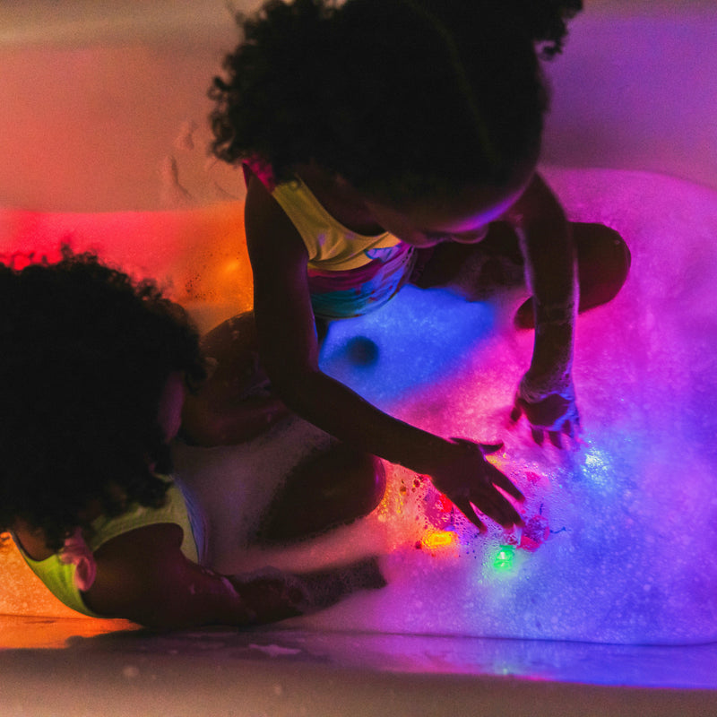 Two children playing with colorful glowing Glo Pals light-up bath toys in water