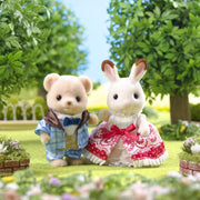Two Sylvanian Families figures - bear in blue outfit and rabbit in red dress in garden setting