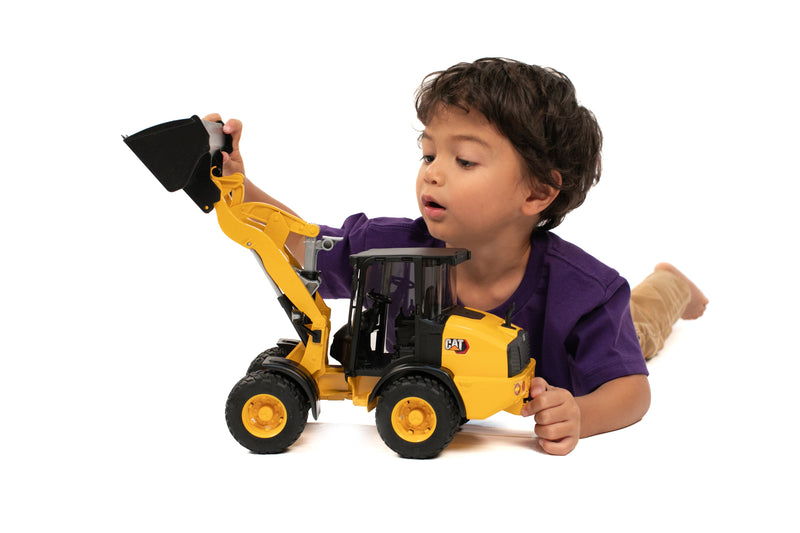 Child playing with yellow CAT wheel loader toy truck by Bruder