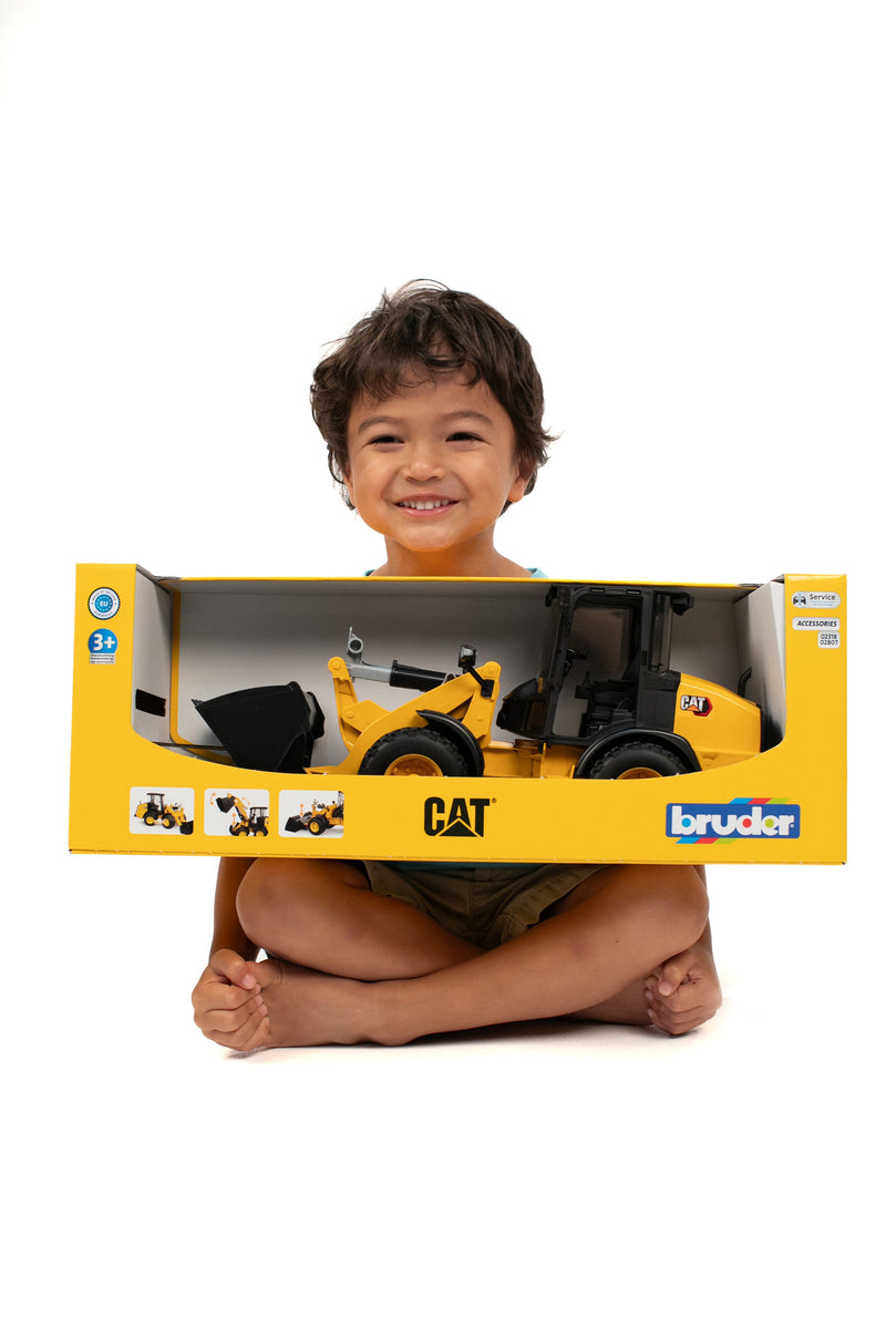 Happy child holding CAT Wheel Loader toy in Bruder packaging box