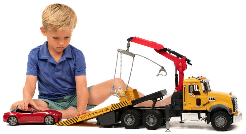 Young boy playing with Bruder MACK Granite tow truck and red roadster toy set