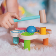 Child using wooden mallet to hammer colorful pegs on Goki hammer bench toy