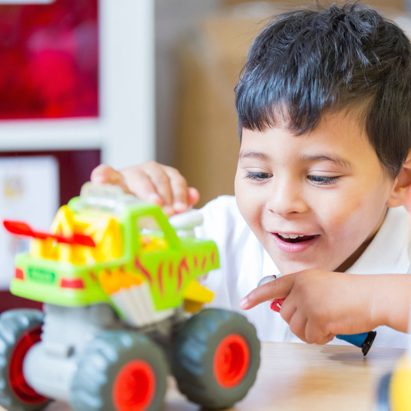 Young boy smiling while playing with a colorful green and yellow Monster Truck toy