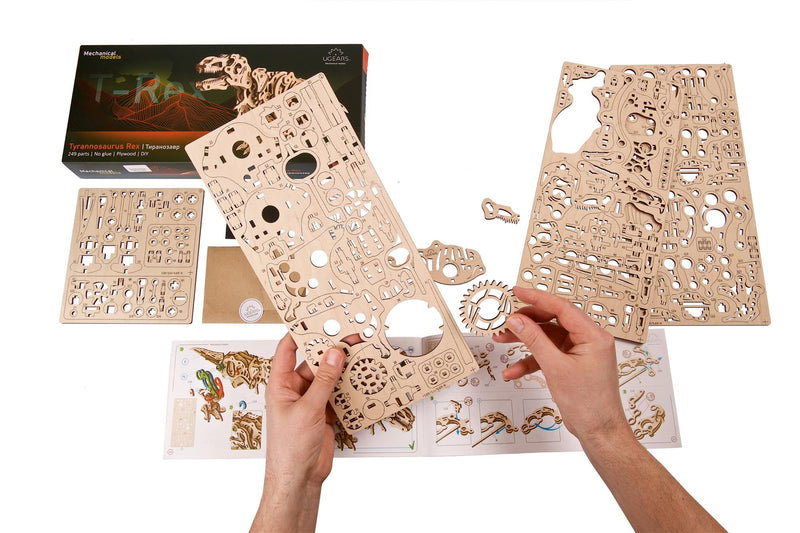 Hands assembling wooden Tyrannosaurus Rex mechanical puzzle kit with laser-cut pieces and instruction manual