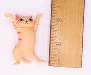 Small cream colored cat figurine with pink ears and orange stripes shown next to ruler for size