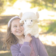 Young girl holding white fluffy Highland Cow plush toy in natural outdoor setting