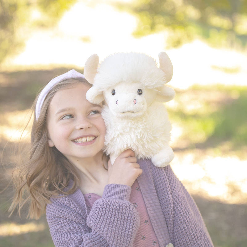 Young girl holding white fluffy Highland Cow plush toy in natural outdoor setting