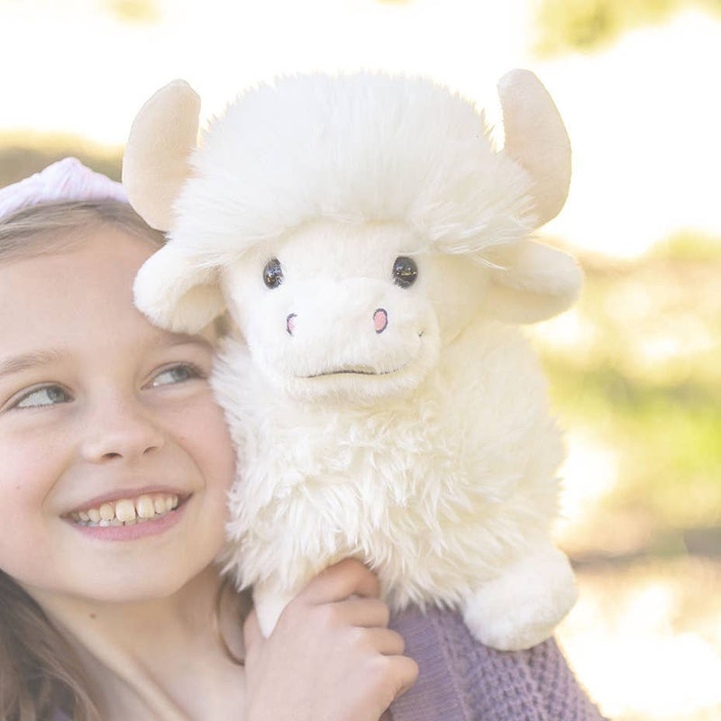 Child hugging white fluffy Highland cow plush toy outdoors in sunlight