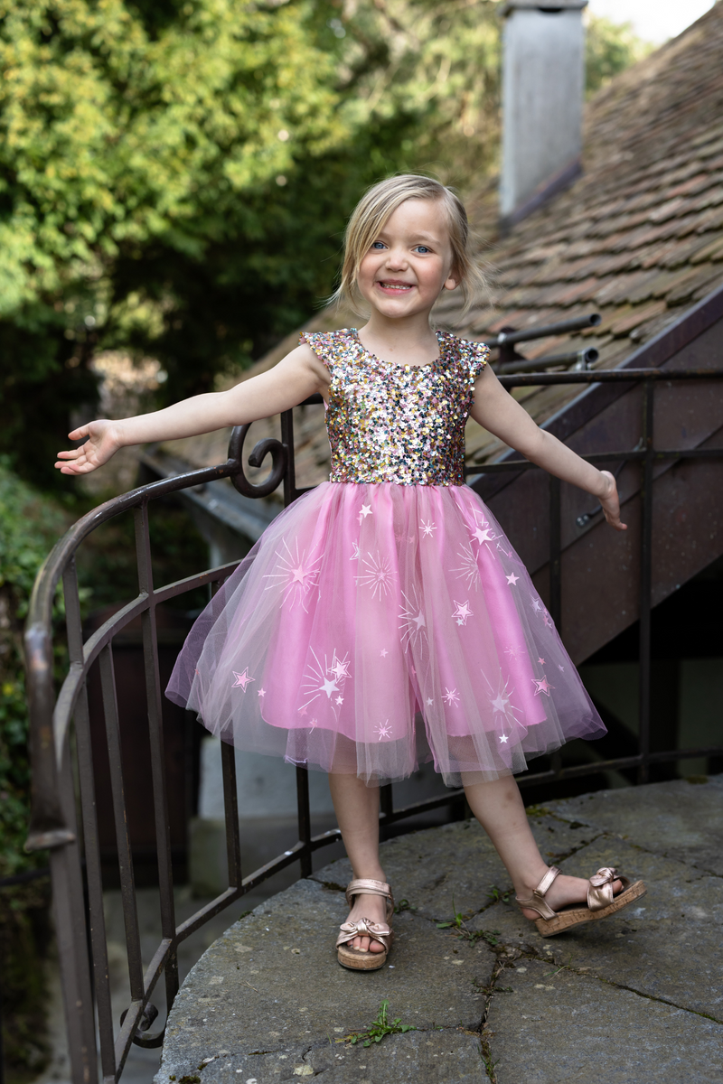 Young girl wearing sparkly sequined bodice dress with pink tulle skirt decorated with stars