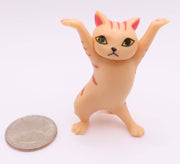 Small peach colored dancing cat figurine with arms raised shown next to quarter for size reference