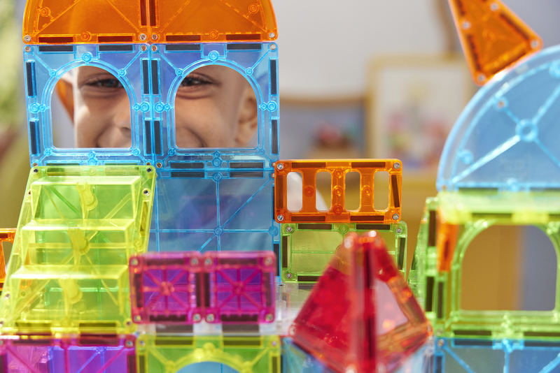 Child playing with colorful translucent Magna-Tiles magnetic building blocks in various shapes