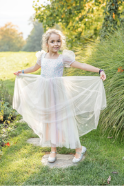Young girl wearing sparkly rainbow tulle dress with puffy sleeves in garden setting