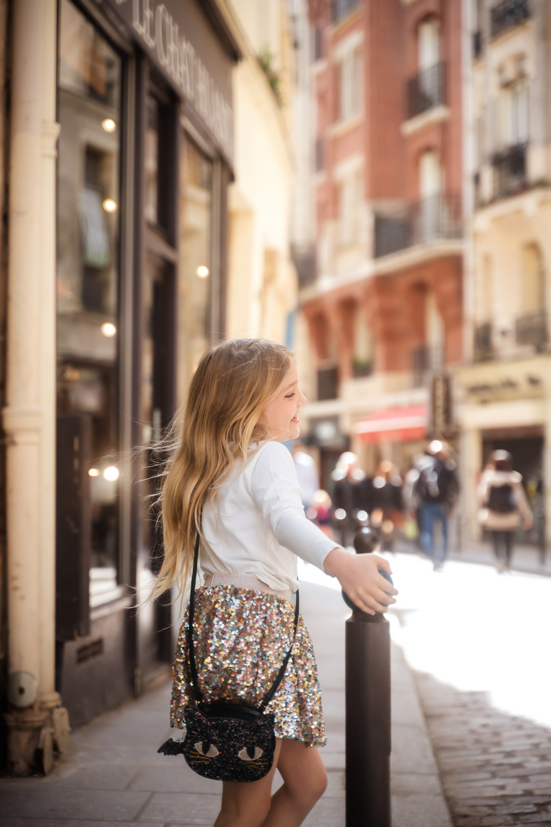Young girl wearing black glitter cat purse with sequined skirt in urban street setting