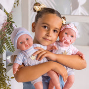 Child holding two Berenguer 15 inch twin baby dolls in striped outfits