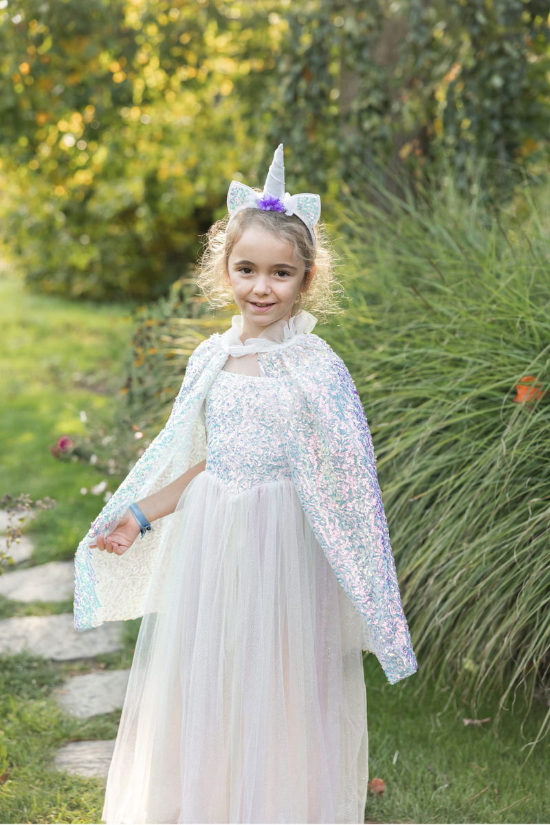 Young girl wearing sparkly rainbow sherbet unicorn dress with cape and horn headband outdoors