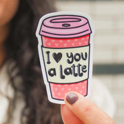 Hand holding pink coffee cup vinyl sticker with 'I love you a latte' text