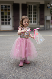 Young girl wearing pink sequined dress with tulle skirt and star wand outdoors