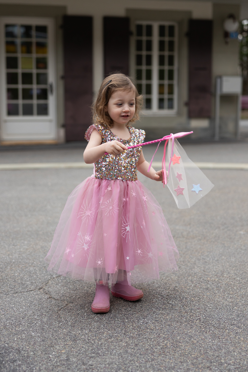 Young girl wearing pink sequined dress with tulle skirt and star wand outdoors