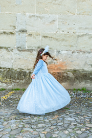 Girl in light blue princess dress twirling on cobblestone street
