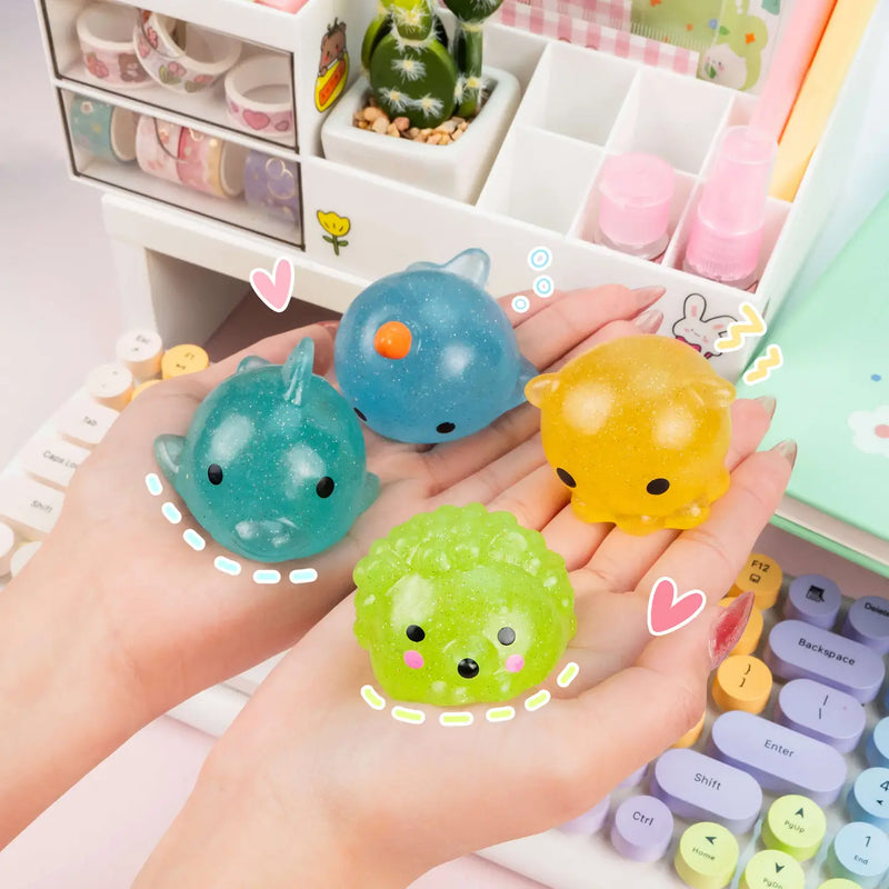 Four colorful glitter mochi squishy toys held in hands on kawaii desk setup