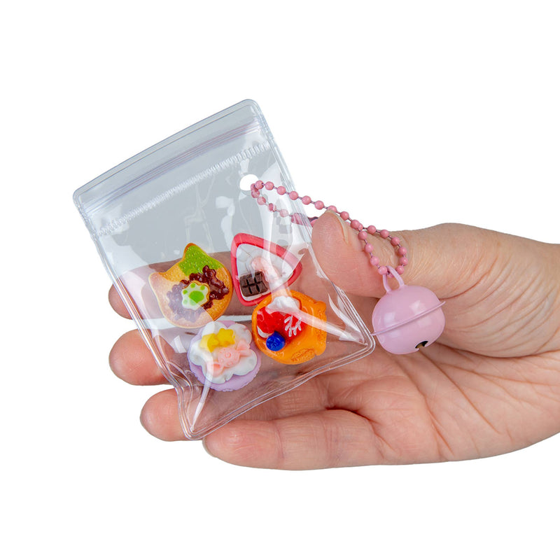 Hand holding clear pouch containing miniature food charms with pink beaded strap