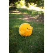 Yellow fluffy chick plush toy sitting on green grass outdoors