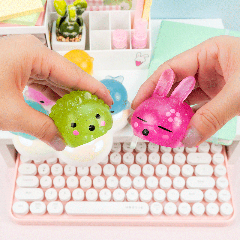 Hands holding colorful glitter mochi squishy toys above pink keyboard in kawaii workspace