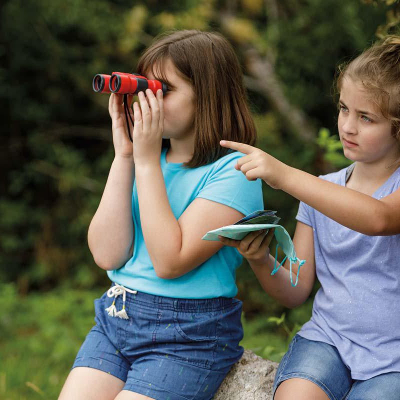 Two children using red binoculars outdoors for bird watching activity