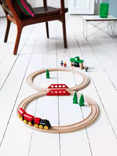 Wooden figure-8 train track set with red train and bridge on white floor