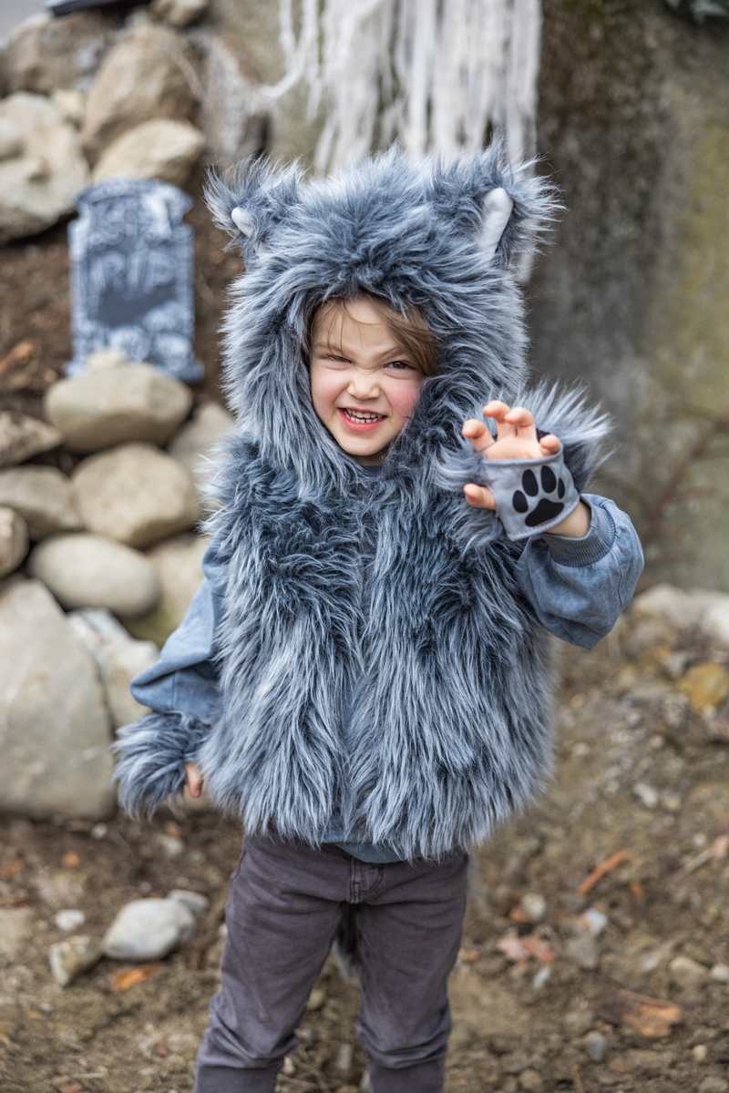 Child wearing gray furry wolf costume vest with hood and paw gloves outdoors