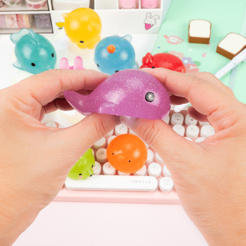 Hands holding purple glittery whale-shaped mochi squishy toy with other kawaii squishies in background