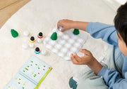 Child playing with Snow Problem puzzle game showing game pieces and challenge book