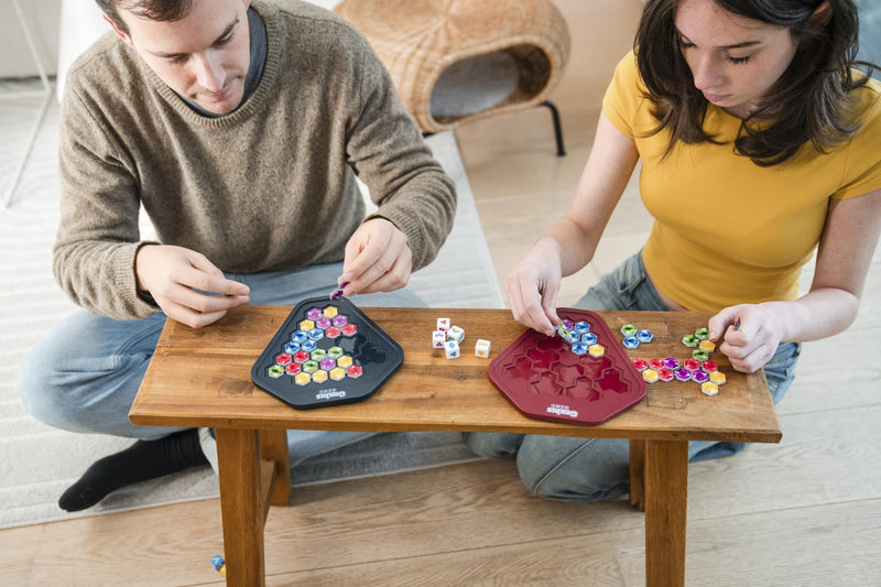 Two people playing Genius Gems puzzle game with colorful hexagonal tiles on wooden table