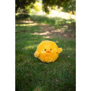 Yellow fluffy chick plush toy sitting on grass in outdoor garden setting