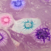 Colorful mini bath bombs dissolving in water creating cosmic purple and blue swirls