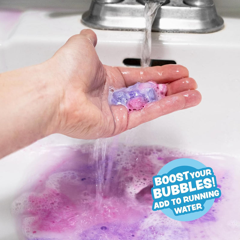 Hand holding colorful mini bath bombs under running water creating purple bubbles