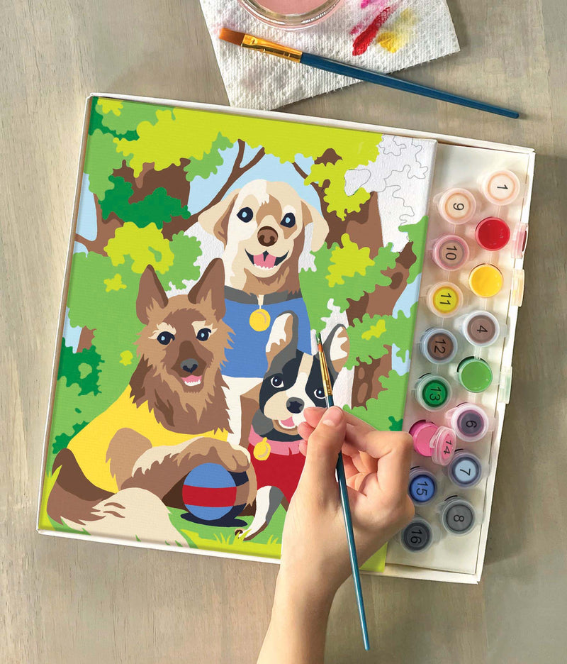 Person painting Dogs' Day Out paint by numbers kit showing three dogs in park setting
