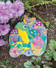 Colorful painted garden stone with frog, butterfly, mushrooms and flowers displayed in garden setting