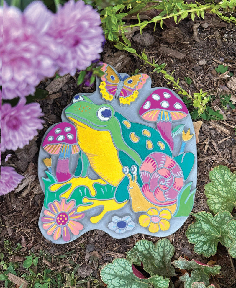 Colorful painted garden stone with frog, butterfly, mushrooms and flowers displayed in garden setting