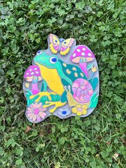 Colorful painted garden stone with frog, butterfly, mushrooms and flowers on grass