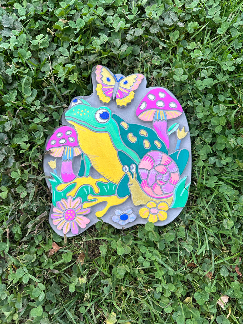 Colorful painted garden stone with frog, butterfly, mushrooms and flowers on grass