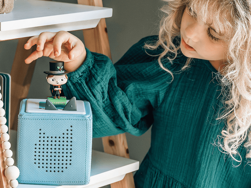 Child playing with Tonie figure on blue audio player showing Christmas Carol character
