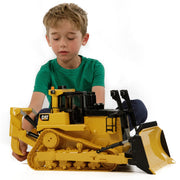 Young boy playing with large yellow CAT track-type tractor toy on white background
