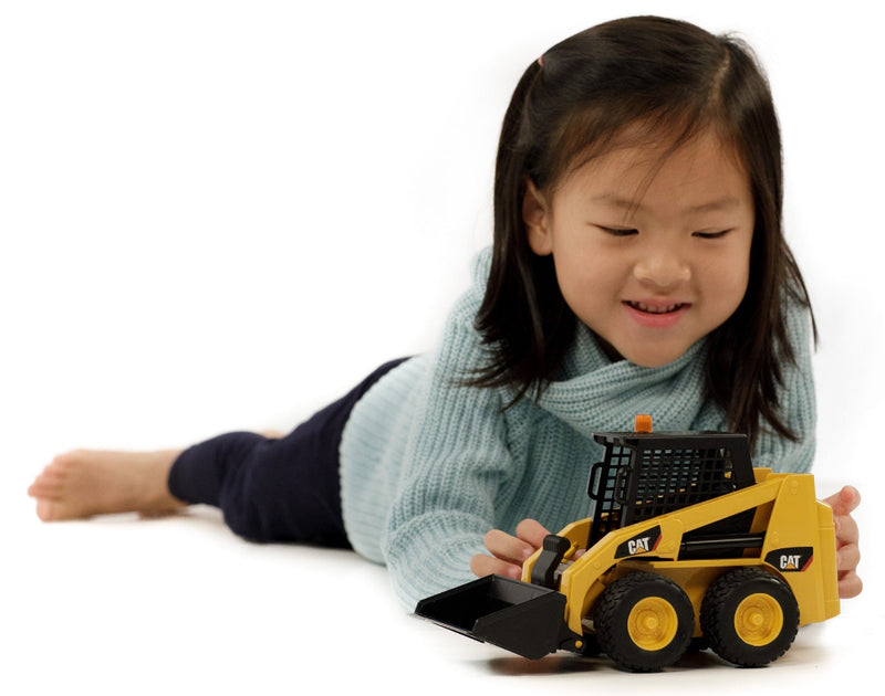 Young girl lying on floor smiling while playing with CAT skid steer loader toy