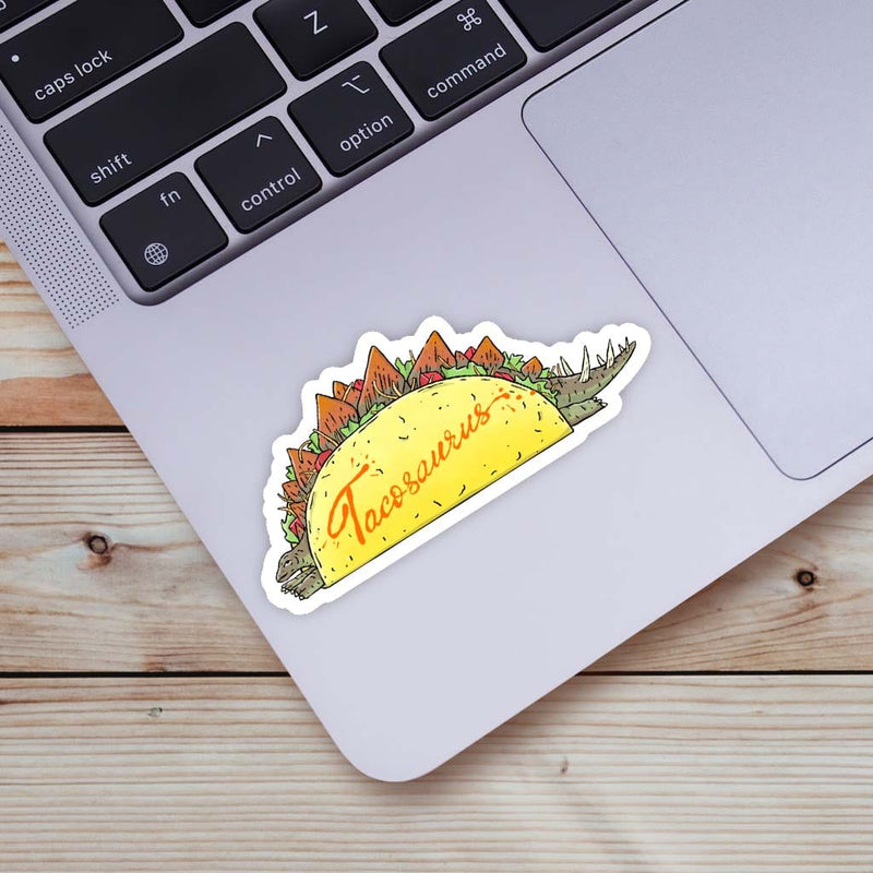 Taco-saurus vinyl sticker on laptop showing stegosaurus dinosaur shaped like taco