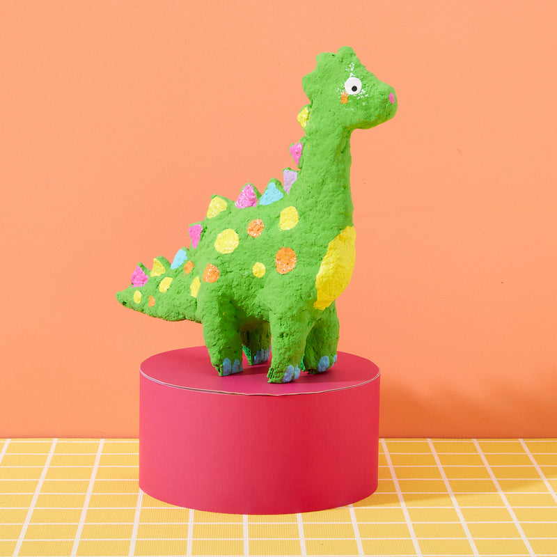 Green paper mache dinosaur craft with colorful spots on pink pedestal