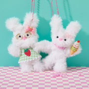 Two white fluffy bunny keychains with accessories on checkered surface