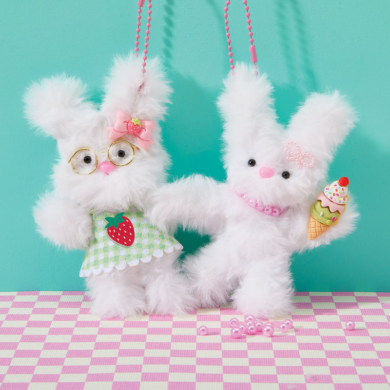 Two white fluffy bunny keychains with accessories on checkered surface