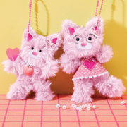 Two pink chenille cat plushies with heart accessories and glasses on checkered surface
