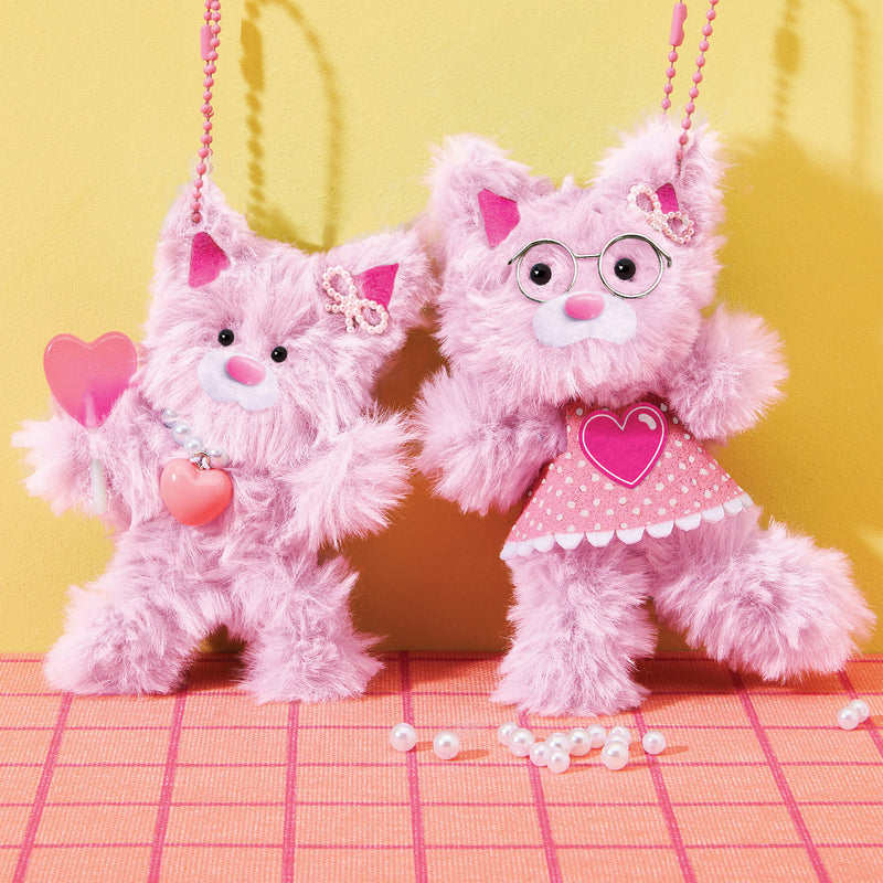 Two pink chenille cat plushies with heart accessories and glasses on checkered surface